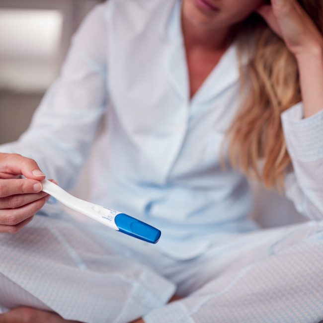 Close Up Of Unhappy Woman Wearing Pyjamas In Bedroom Holding Pregnancy Test